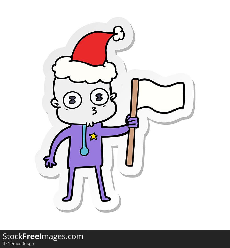 sticker cartoon of a weird bald spaceman with flag wearing santa hat