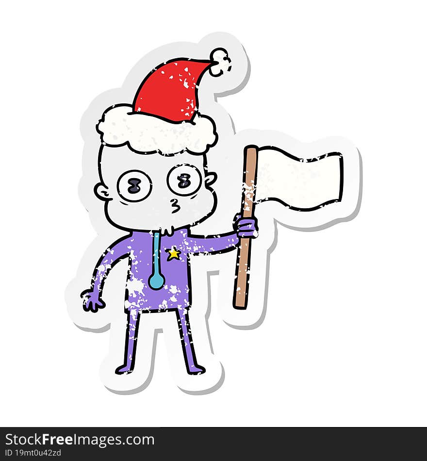 distressed sticker cartoon of a weird bald spaceman with flag wearing santa hat