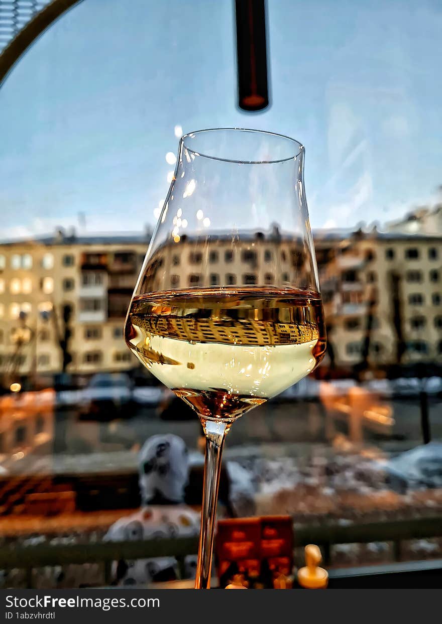 A glass of white wine in front of a window from a restaurant overlooking the city