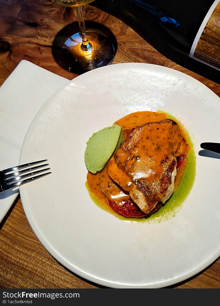 Fish with sauce in a white round plate on the table with wine