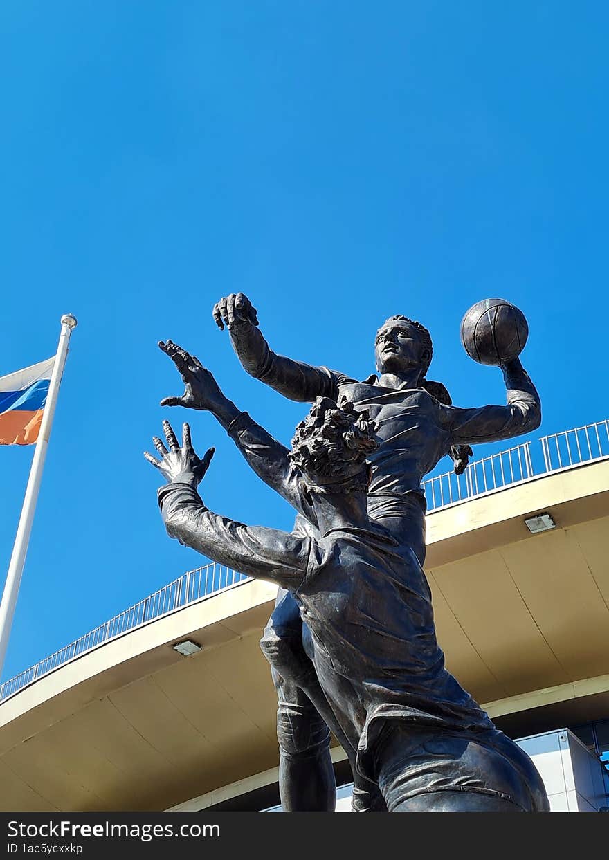 Dark monument to two female volleyball players under bright blue sky