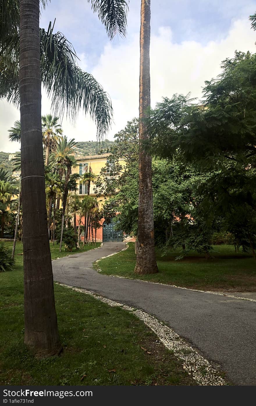 Old mansion in an open space of a park framed by trees and a path on a sunny day