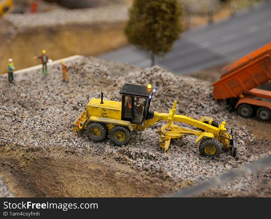 A small grader produsing tiny roadworks at toy maket of a town