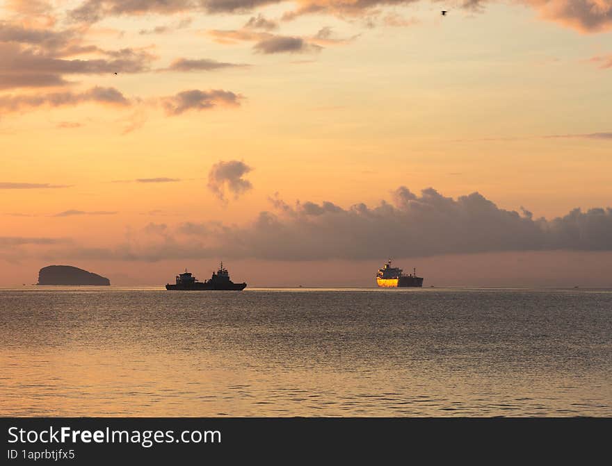 Cargo ships on the horizon of a quiet calm ocean in the dawn or sunset rays of the sun