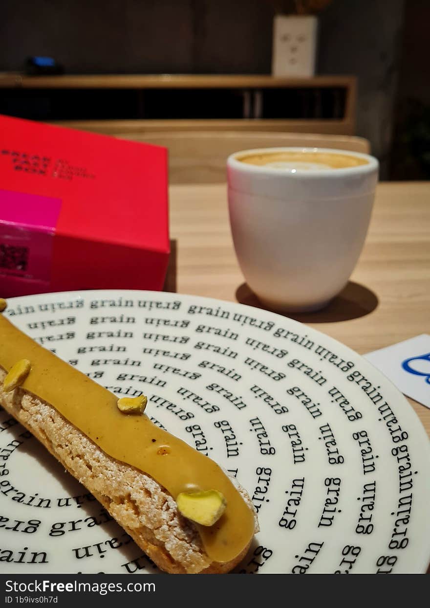 Pistachio eclair on a plate and a cup of coffee