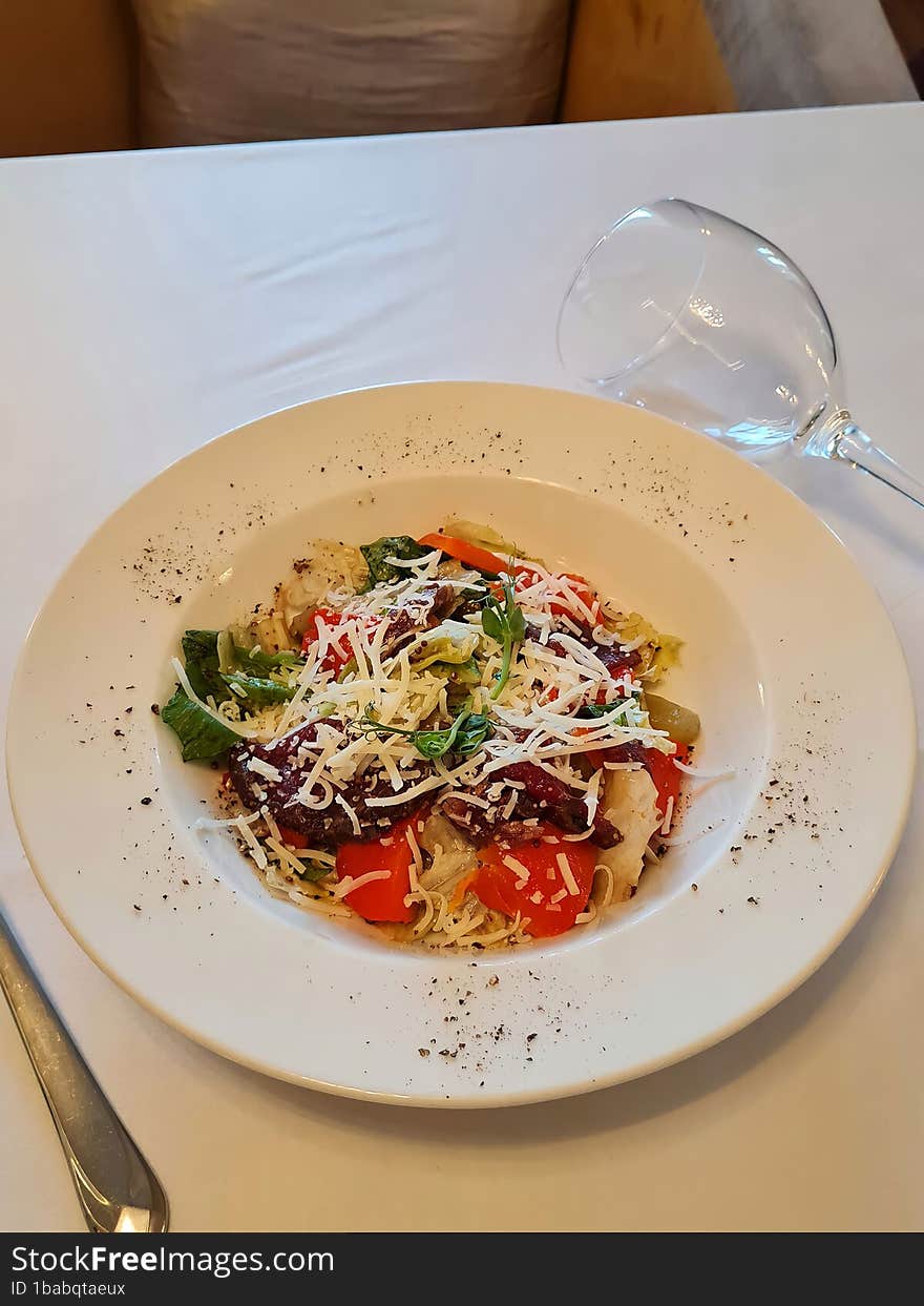 Salad with cheese, vegetables and a glass of wine on a white table