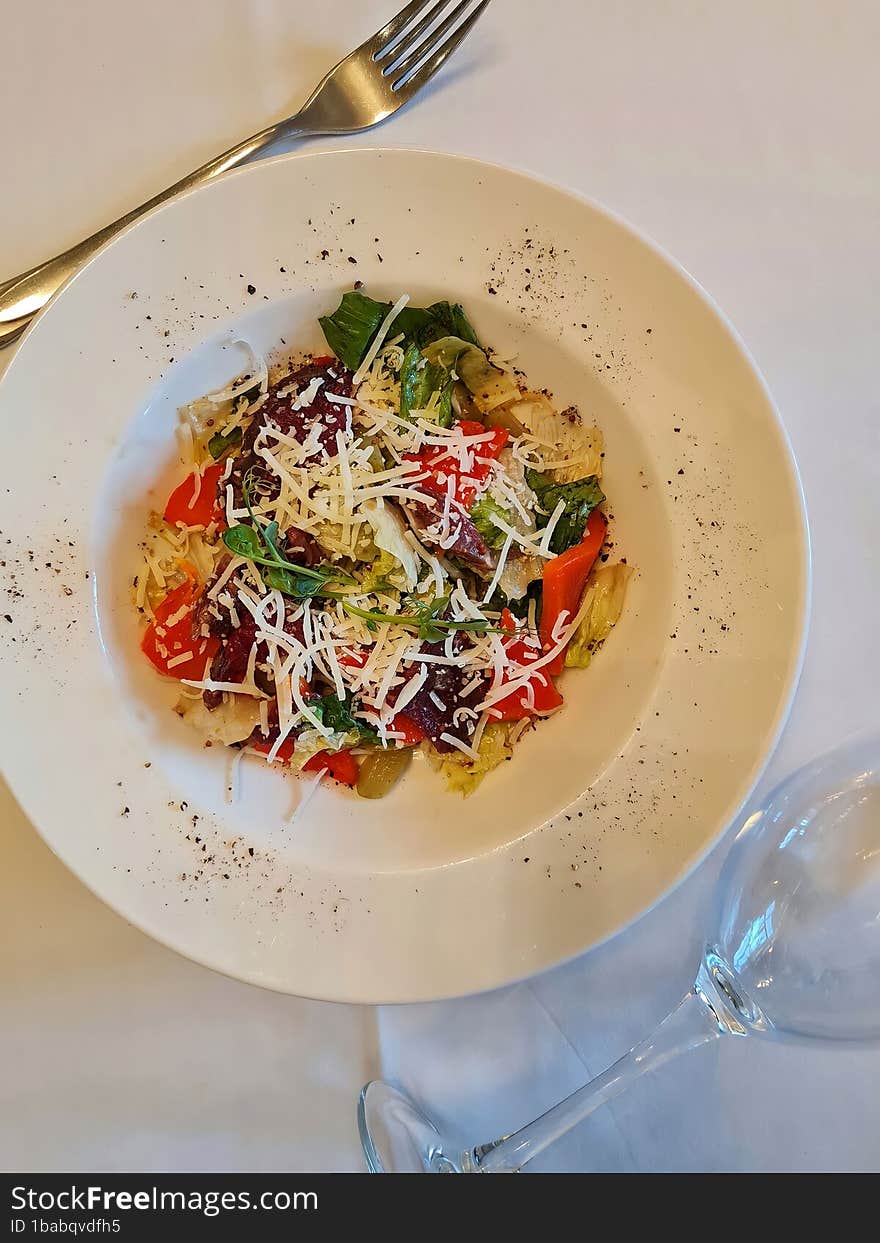 Salad with cheese, vegetables and a glass of wine on a white table