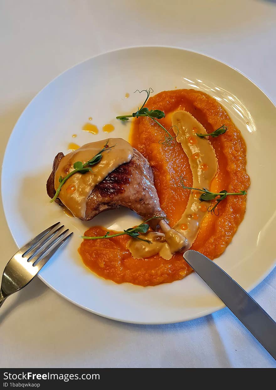 Chicken leg with pumpkin sauce on a white round plate