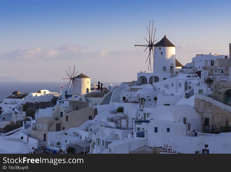 Santorini - Oia, view of white windmills on the slopes of the island. Around are white, picturesque houses between the stone streets. Beautiful sky