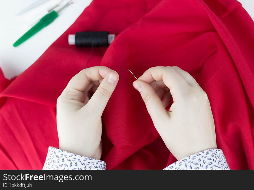 Female hands sews red fabric. A girl holds a needle in her hands. Small business.