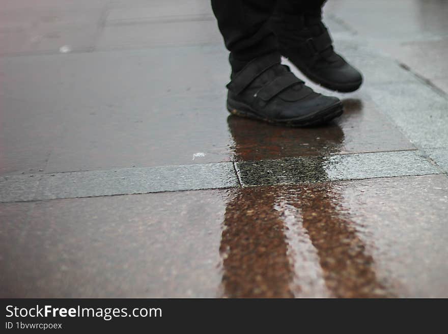 A man stands on wet asphalt in the rain. A park on the seashore. A muddy reflection on the ground.