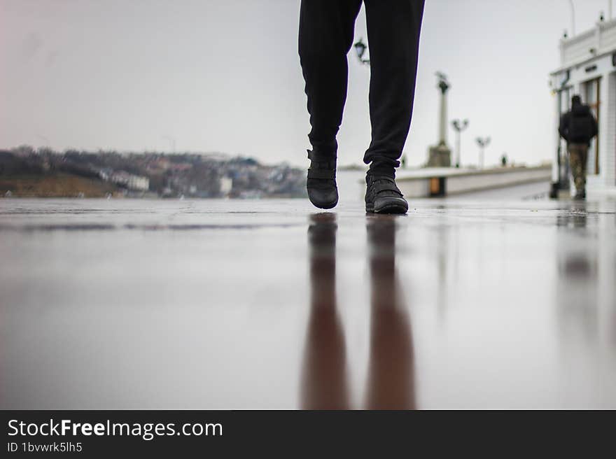 A man walks on wet asphalt in the rain. A park on the seashore. A muddy reflection on the ground.