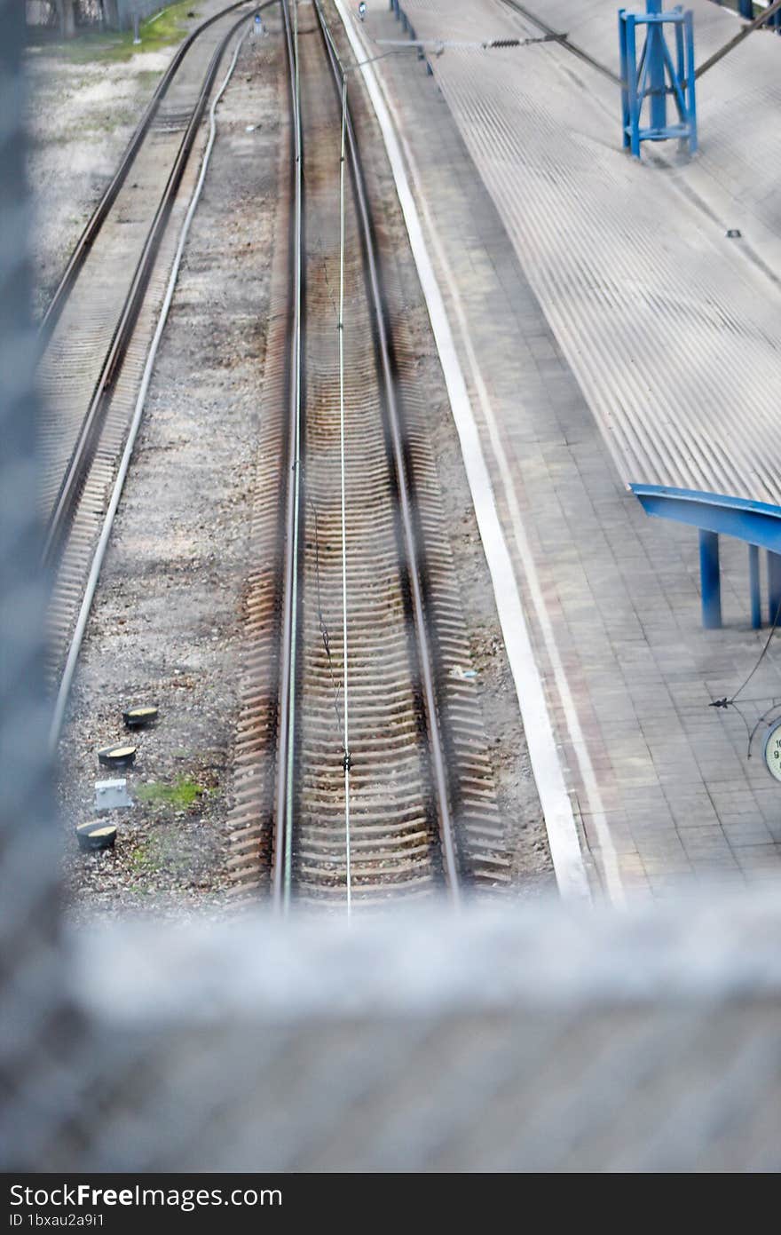 View through the metal fence to the empty platform of the railway station. Blue columns at the railway station.