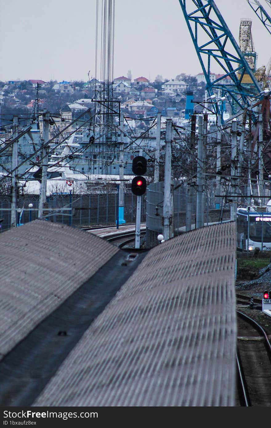 A gloomy view of an empty railway station, behind which there are large port cranes in rust. Grey landscape.