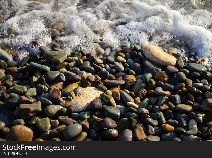 Sea foam from small waves. Crystal clear water on the seashore. The beach is lined with small colorful pebbles.