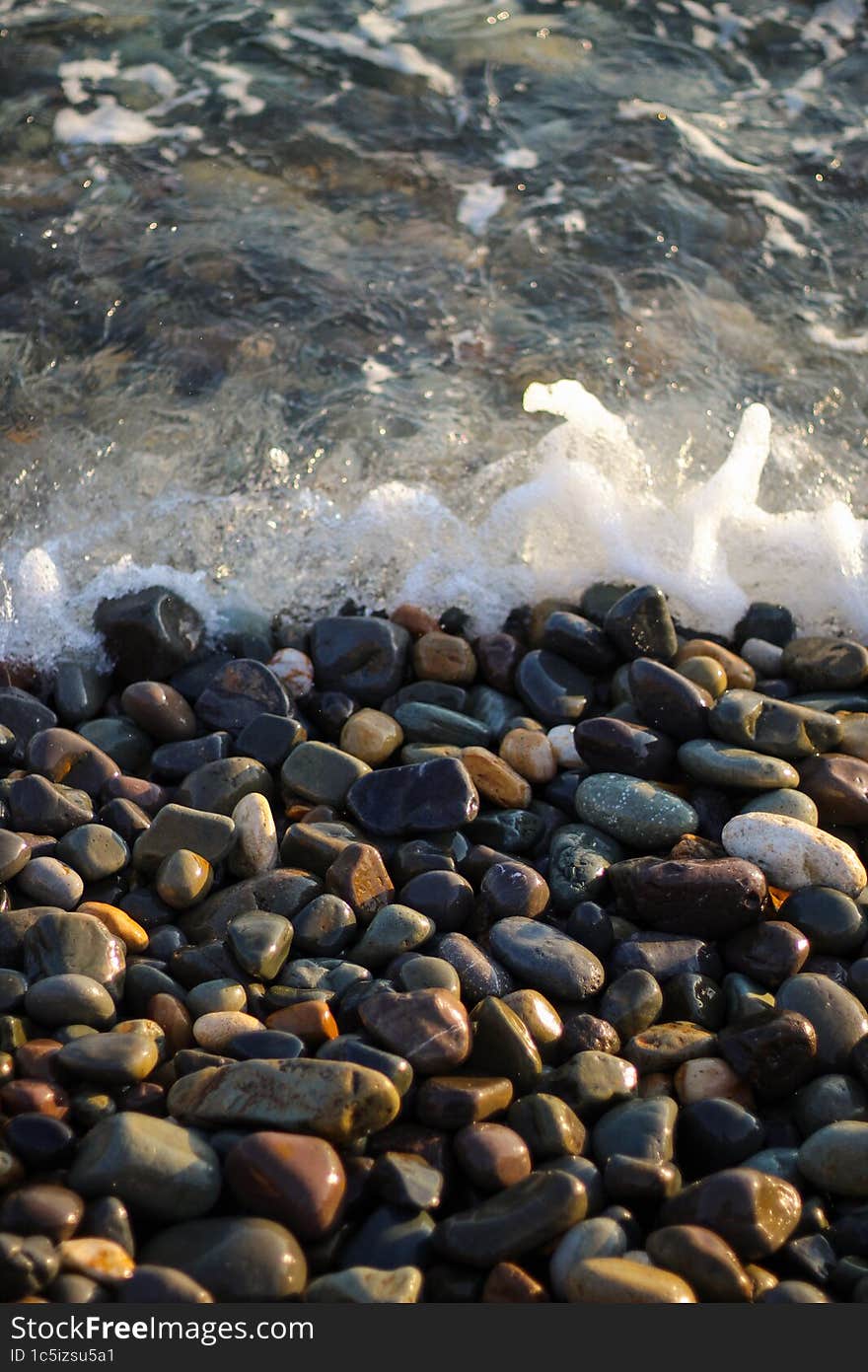 Sea foam from small waves. Crystal clear water on the seashore. The beach is lined with small colorful pebbles.