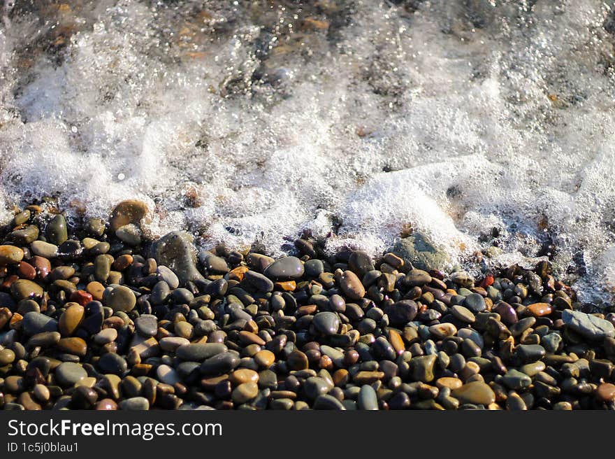 Sea foam from small waves. Crystal clear water on the seashore. The beach is lined with small colorful pebbles.