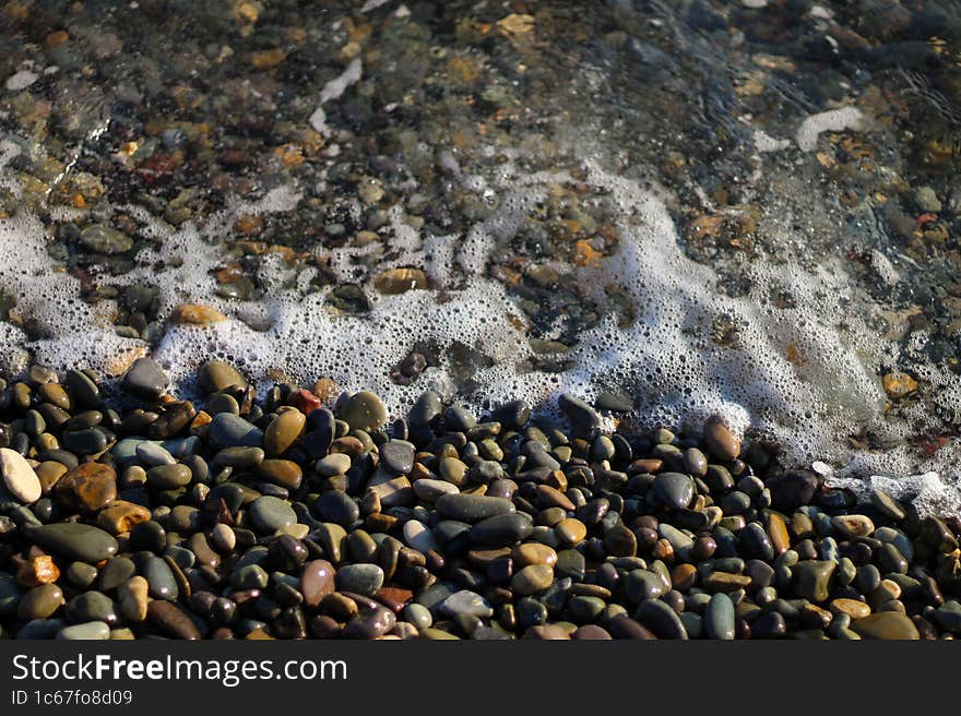 Crystal clear water on the seashore. Sea foam from small waves. The beach is lined with small colorful pebbles.