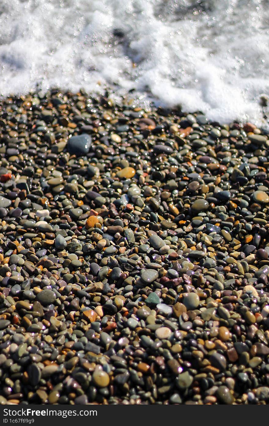 Wet stones by the sea .The beach is linked with small colorful pebbles. Sea foam from small waves.
