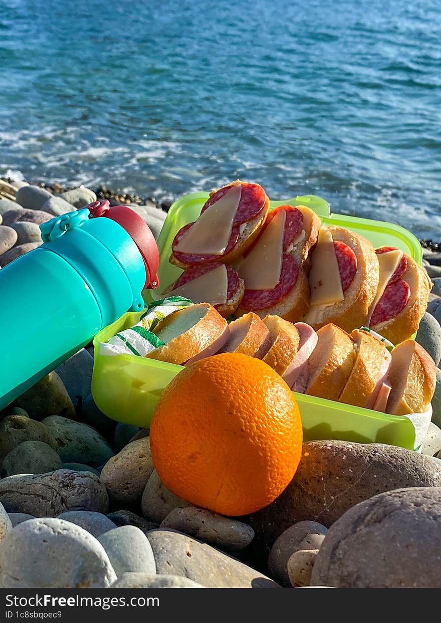 Picnic by the sea. Vacation on the seashore. Sausage and cheese sandwich, as well as tea in a thermos. A beach with a stones.