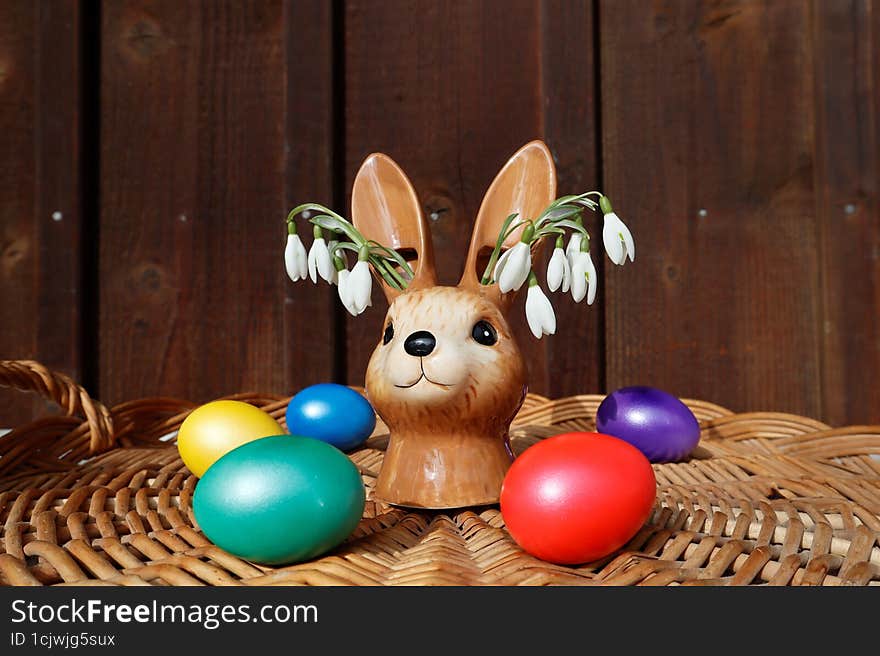A vase in the form of a bunny with snowdrops. The vase stands on a wicker basket on which Easter eggs lie.
