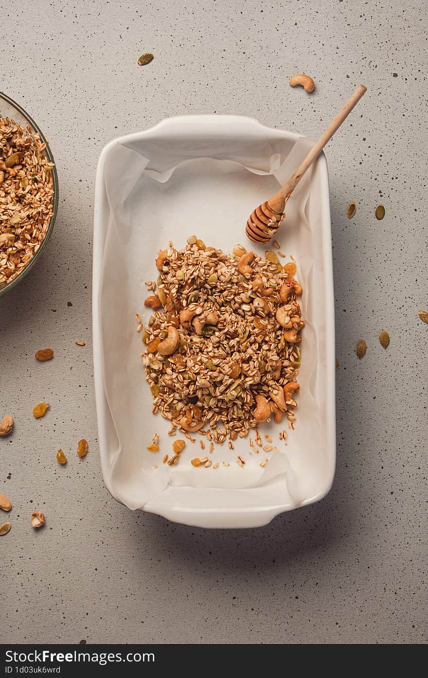 Homemade granola cooking process - oat, cashew nuts, raisins and pumpkin seeds transferring from bowl to baking dish. Healthy brea