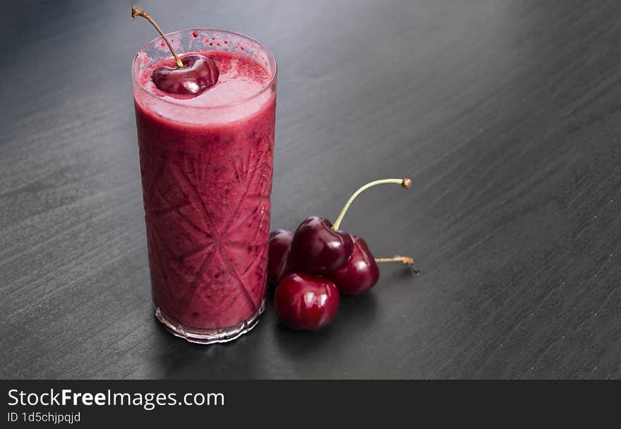 a glass of smoothie made with fresh cherries on dark background