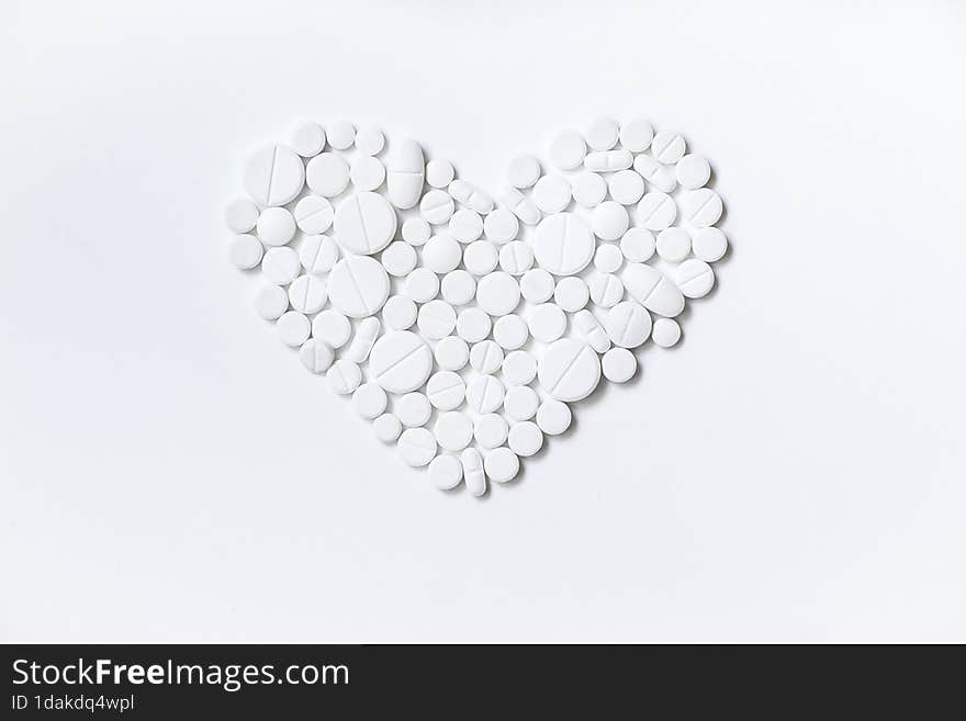 A heart made of tablets of different sizes. White medicines, different shapes, white background.