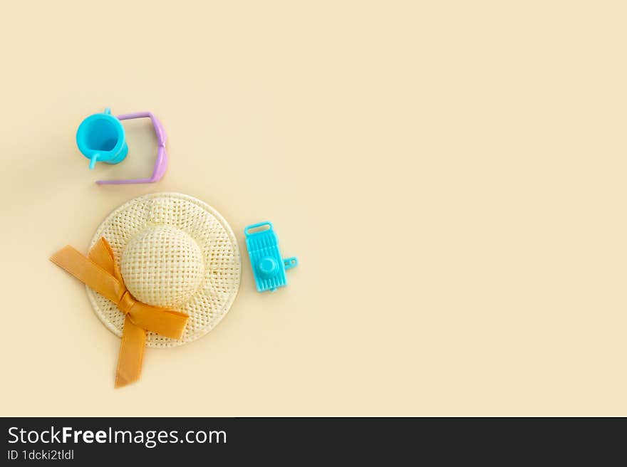 Sunglasses, straw hat, toy camera and toy glass with a straw on a pale beige background, vacation content from copy space