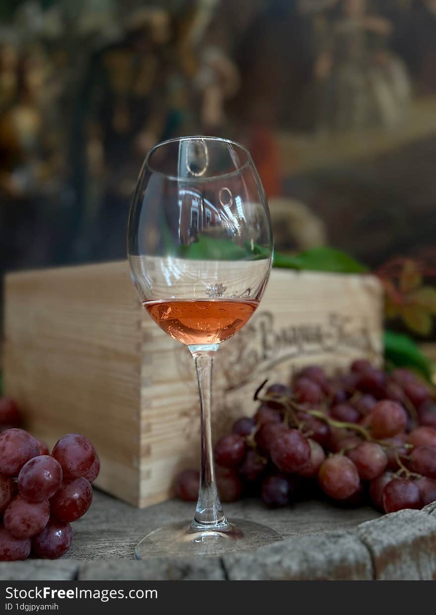 A glass of rose wine on a wooden surface in front of grapes