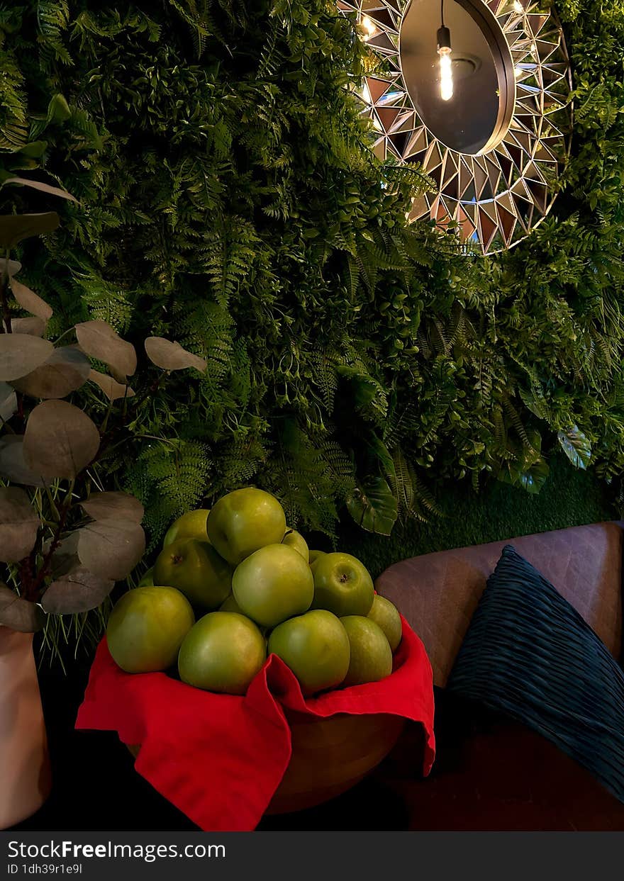 Green apples in a plate near the wall with plants