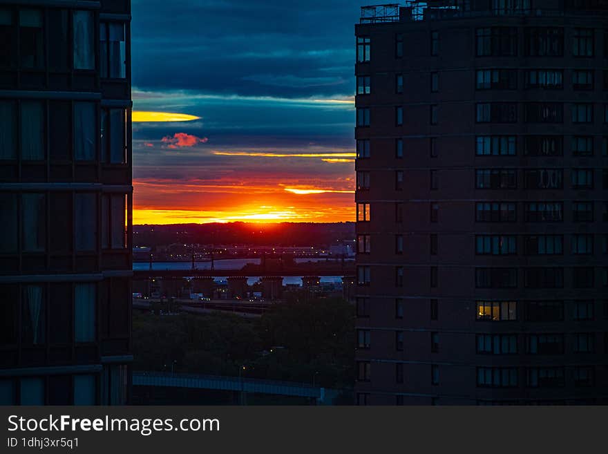 Vibrant orange and red sunrise against dark aquamarine navy blue clouds between two high-rise urban buildings on the upper east si