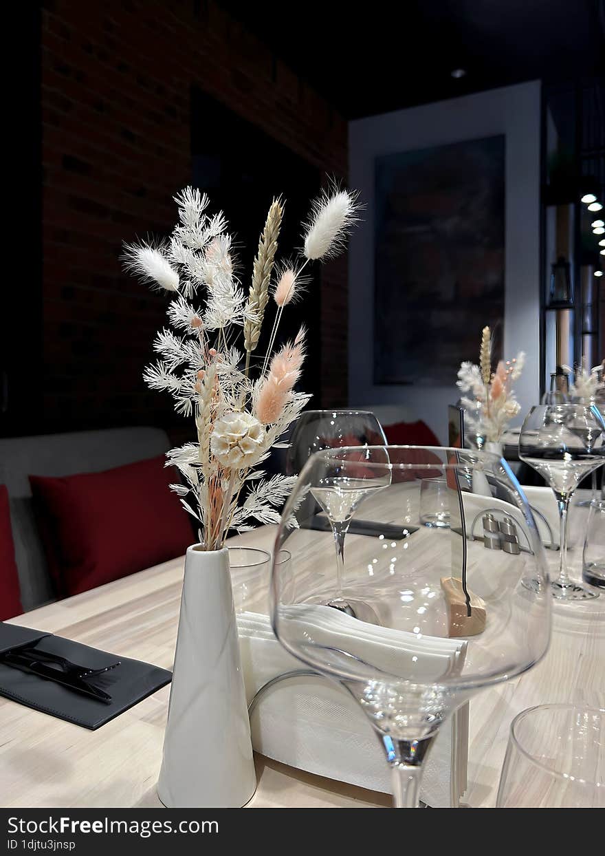 Bouquet of light plants in a white vase on a table with empty glasses