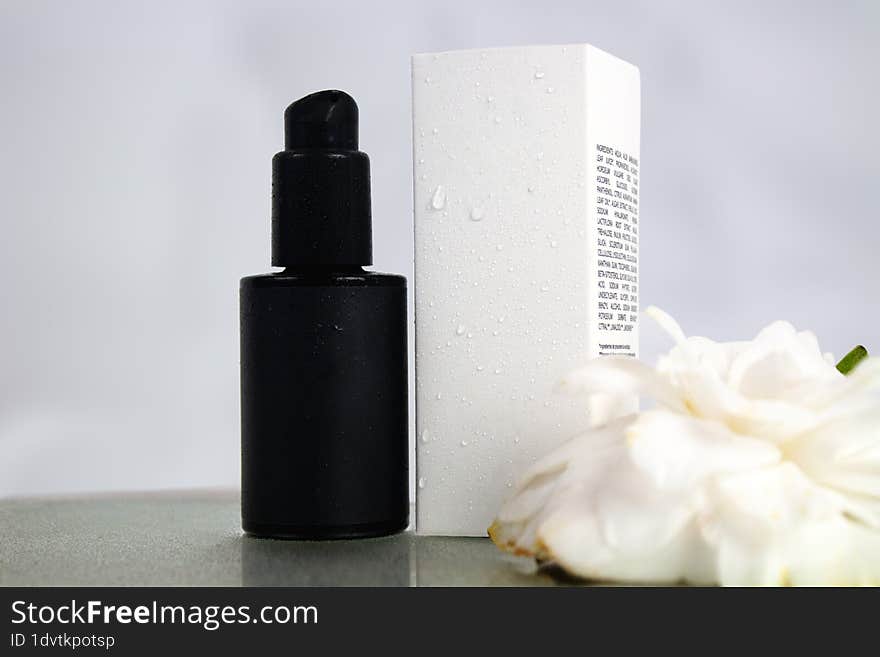 Product photo of black bottle and white box of natural cosmetics, on a white background with camellia flower