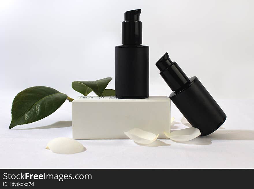 Product photo of white boxes and black jars of natural cosmetics, on a white background with camellia leaves and petals