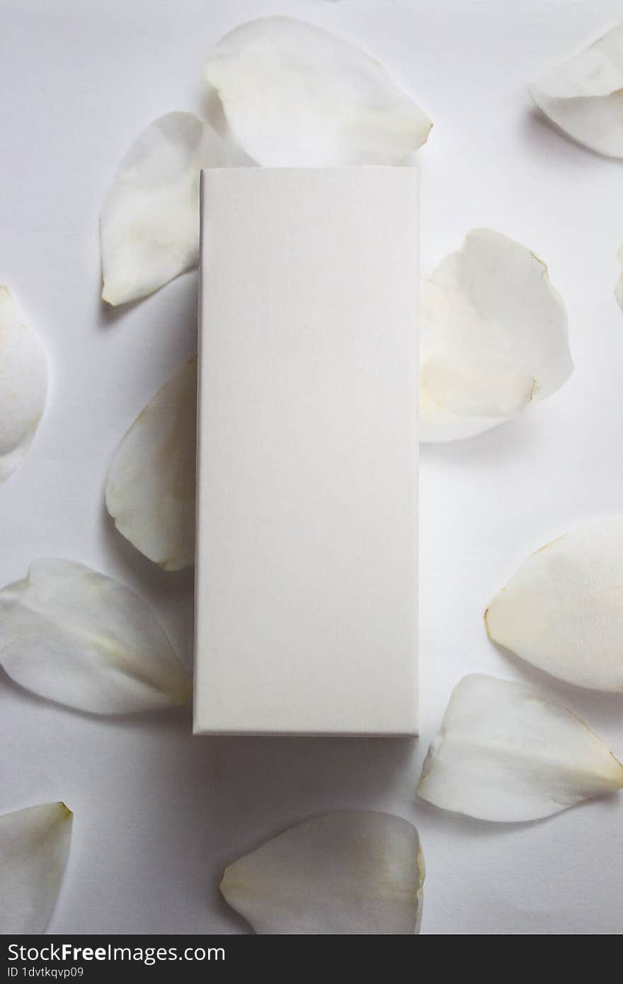 Product photo of a white box of natural cosmetics, on a white background and camellia petals, vertical photo, product photo, for mockups