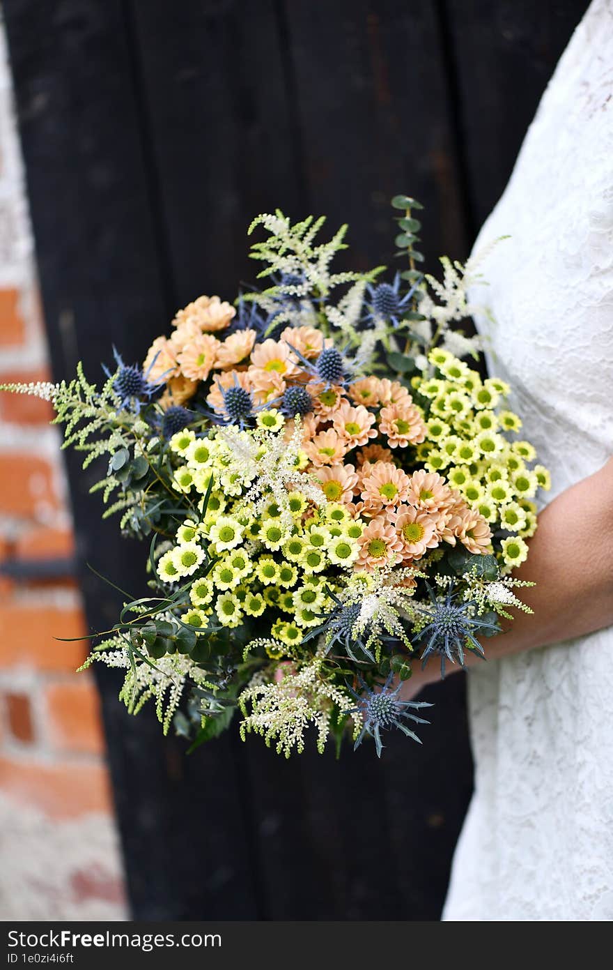 the bride in a white dress holds a large bouquet of yellow and orange meadow flowers with eucalyptus