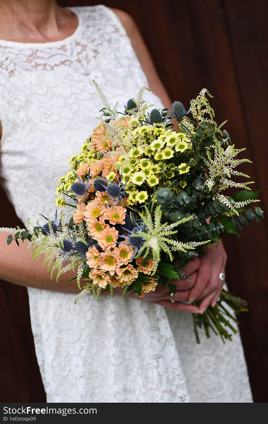 the bride holds a large bouquet of yellow and orange meadow flowers with eucalyptus