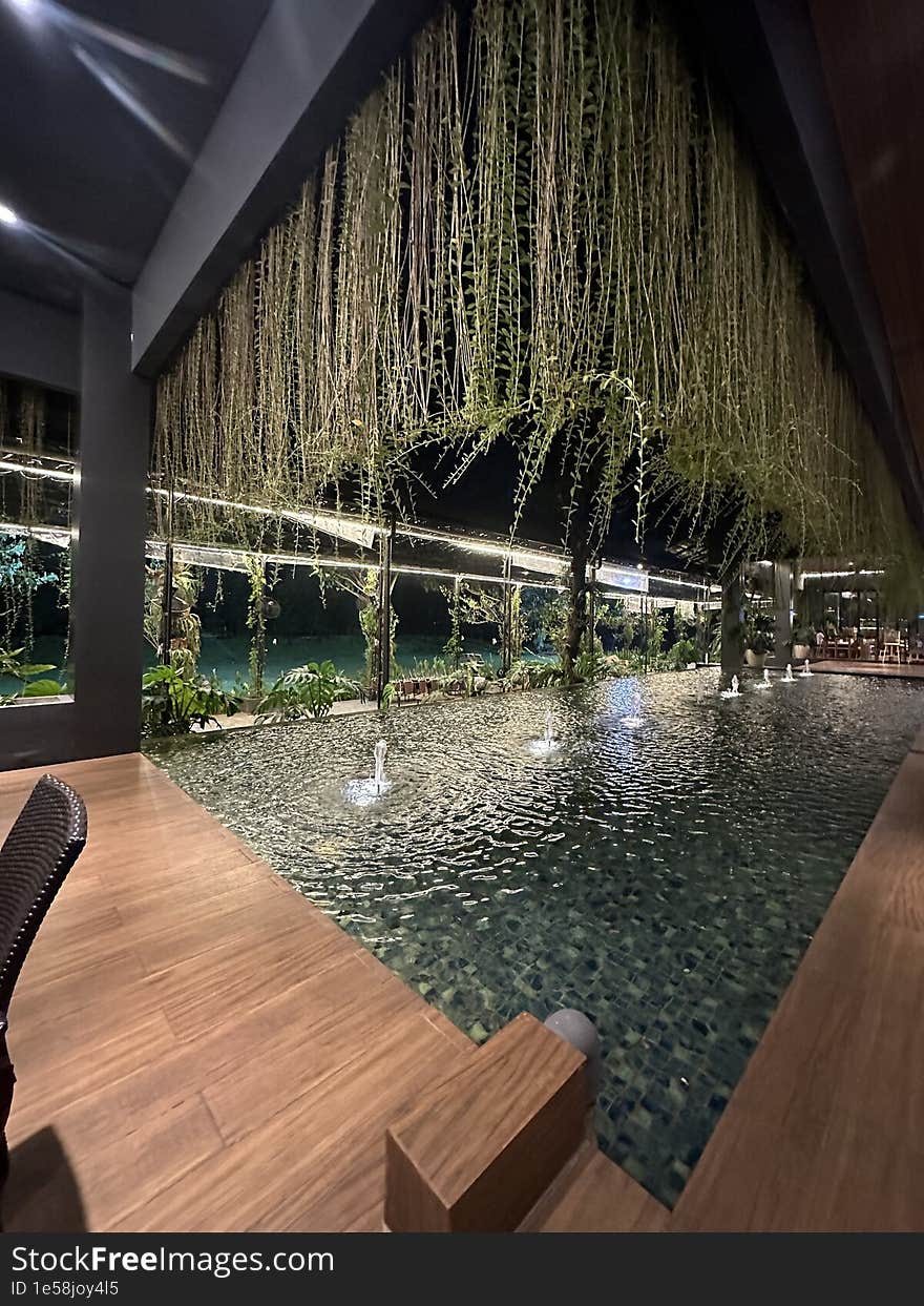 A swimming pool with small water fountains, located indoors in a restaurant in Bintaro, Indonesia. Above it, there are trailing vines adding to the beauty of the ambiance.