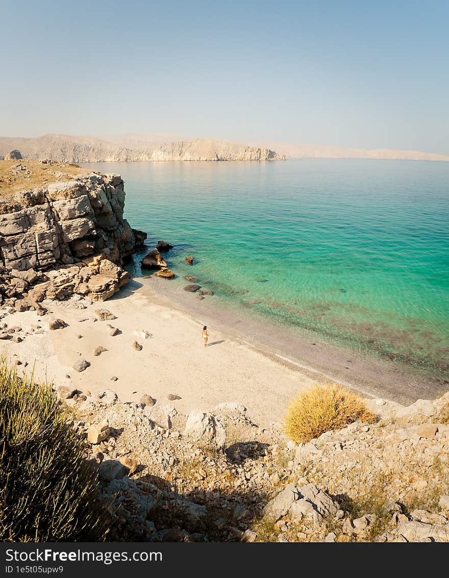 Side panoramic view tourist woman in bikini walk on white sand beach to turquoise water in persian gulf Mirellas island. Musandam.Oman