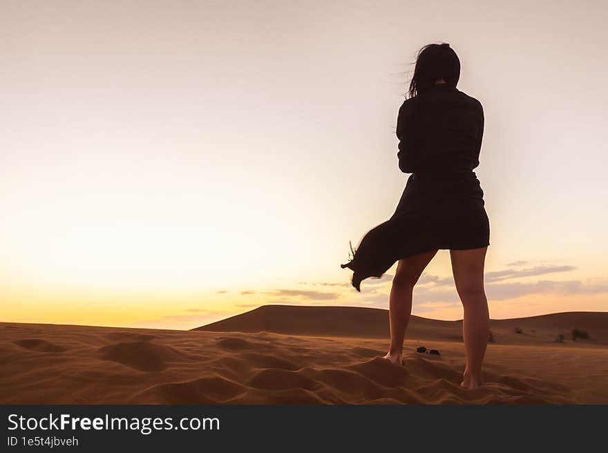 Woman stand enjoy sand dunes in desert watch sunset relax on golden hour alone. Travel lifestyle and wellness concept. Cinematic wanderlust background