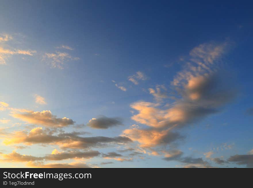 Light cirrus small orange clouds in the blue sky are illuminated by the morning sunlight.