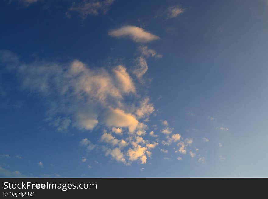 Light cirrus small orange clouds in the blue sky are illuminated by the morning sunlight.