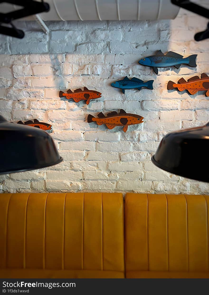 Multi-colored Fish Figures On A White Brick Wall Above A Yellow Sofa