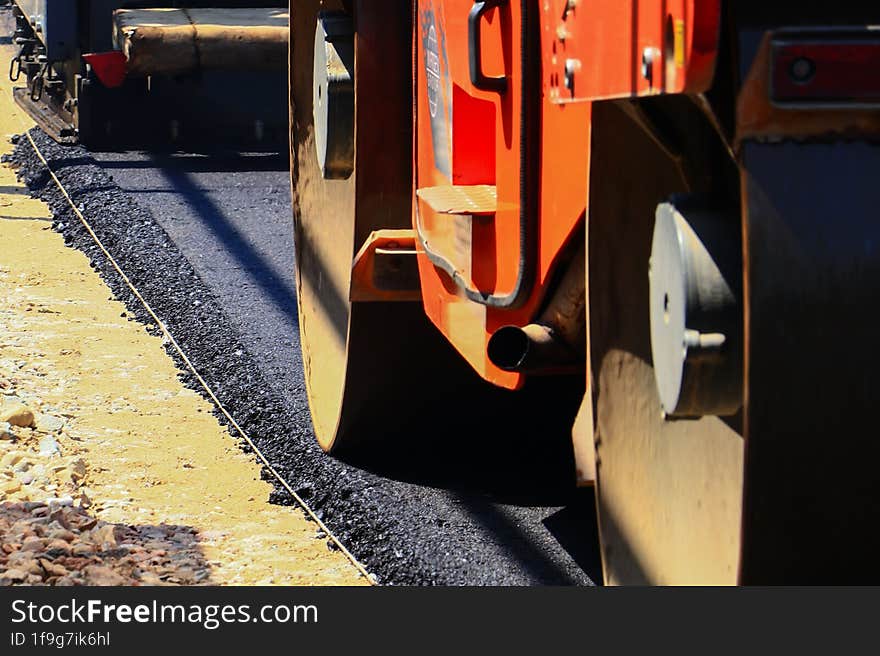 Half blurred paver and roller laying new and fresh asphalt on salt marsh