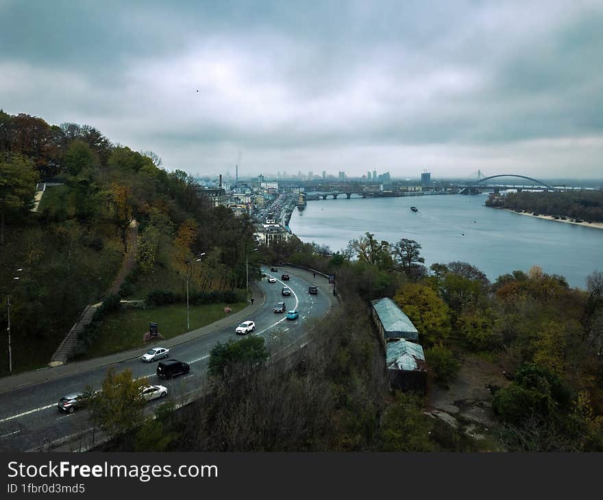 Aerial View of road with passing cars, on hillside against backdrop of river Dnieper and city Kyiv.