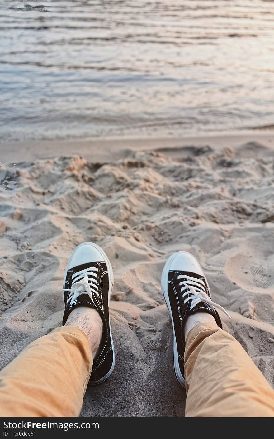 First-person view of men& x27 s feet in sneakers on beach against backdrop of sea. Vacation, summer vacation concept.