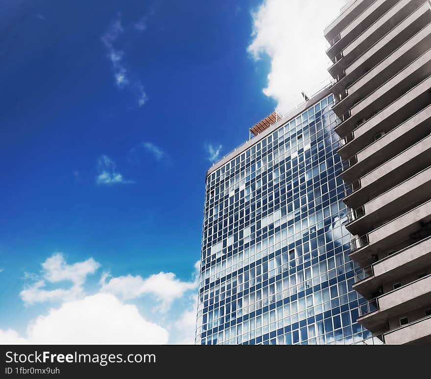 Bottom view of modern office building on background of blue sky with white clouds.