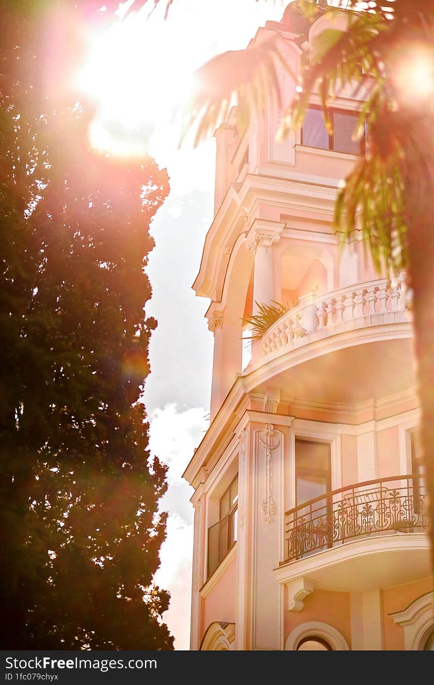 Bottom view of the front facade of a beautiful building against the backdrop of the sun casting glare into the lens.