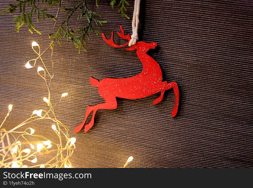 Holiday grey background with coniferous branches, light garland and a wooden figure of a red Christmas deer. Photo with empty space for text and design